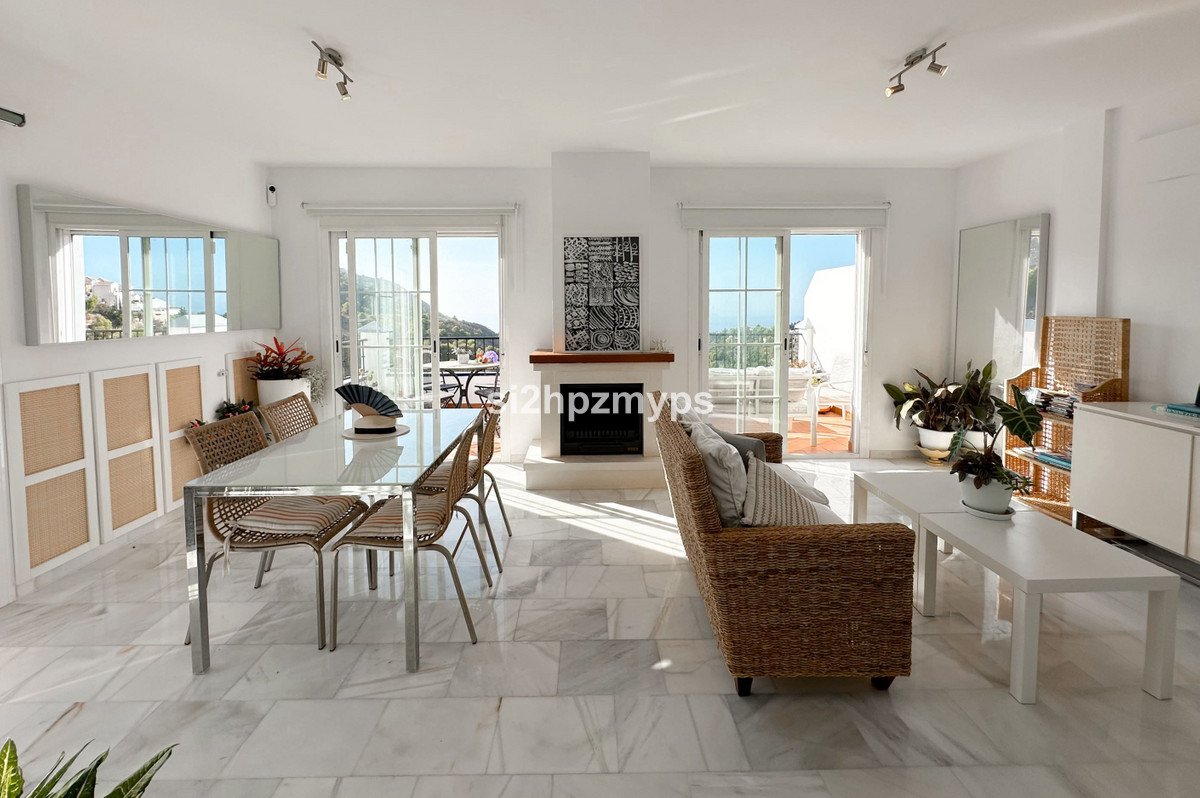 Spacious living and dining area with a fireplace, rattan furniture, and a view of the sea from the terrace.