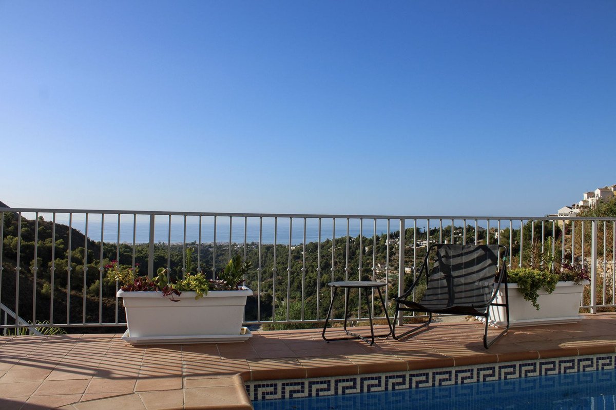 Terrace with poolside seating and planters overlooking the sea and a hillside town on a clear day.
