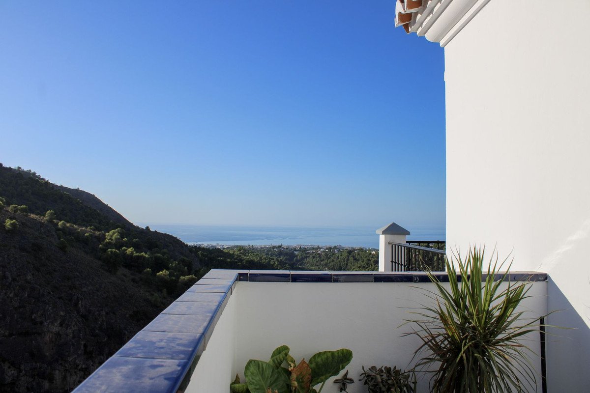 Balcony with tiled railing overlooking a lush green valley, the sea, and hills under a clear blue sky.