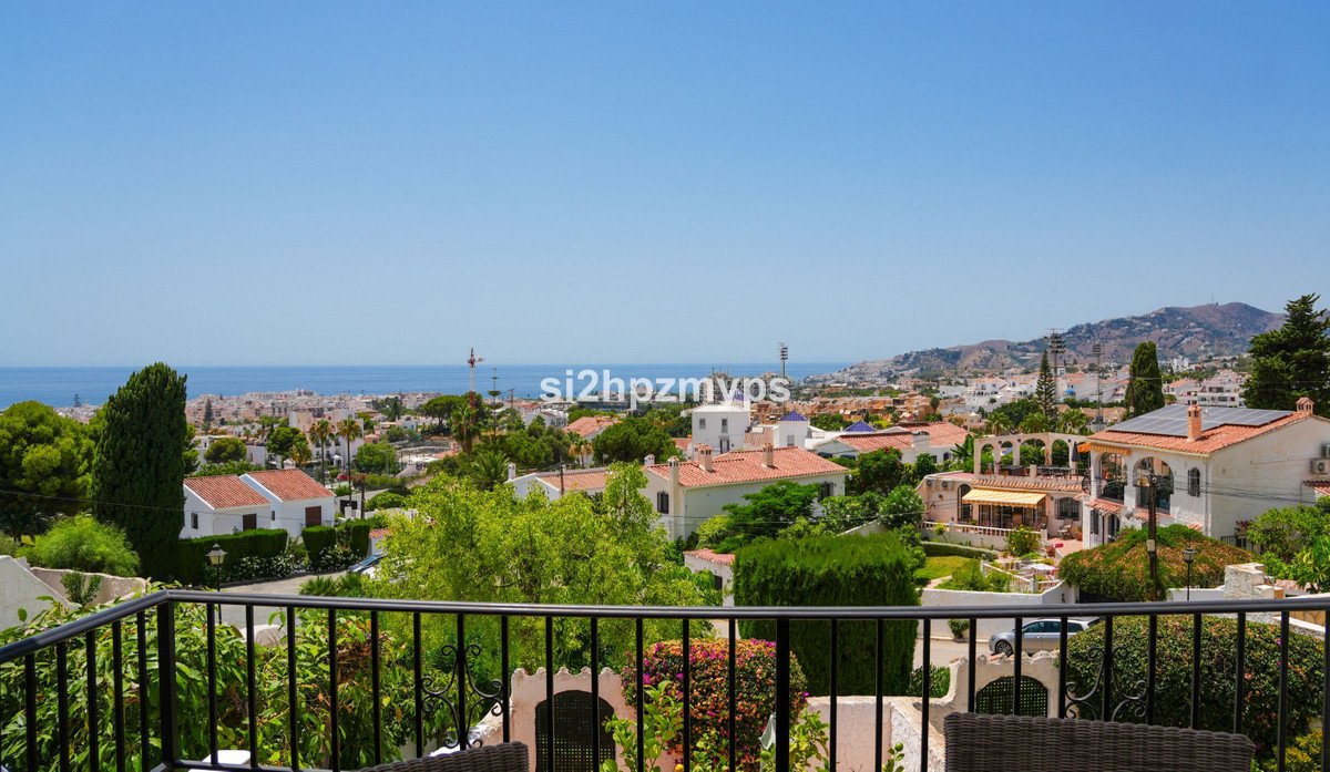 View from a balcony overlooking a town, sea, and mountains on a clear day.
