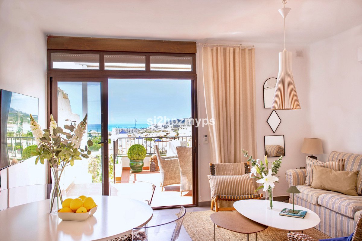 Living room with a sofa, coffee table, and a balcony with a sea view and outdoor seating.