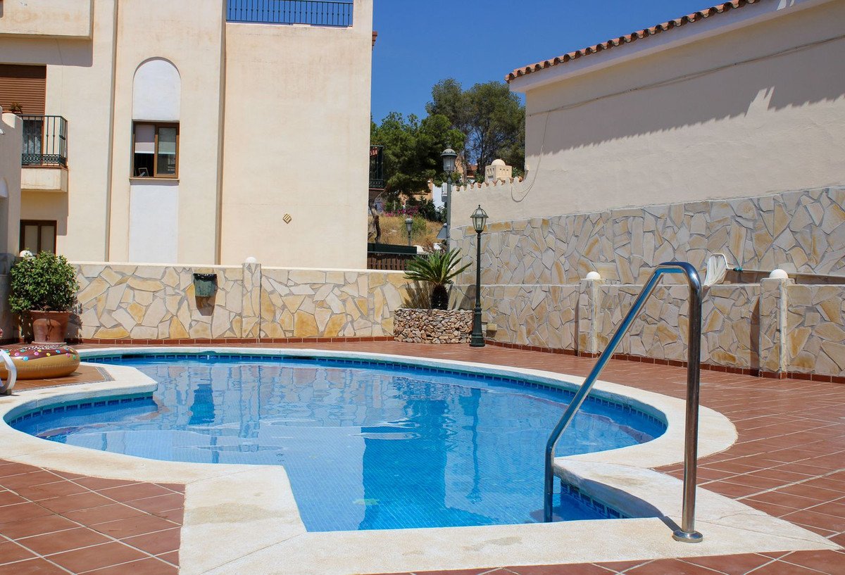 A sparkling blue swimming pool with a metal handrail, surrounded by a stone wall and tiled patio.