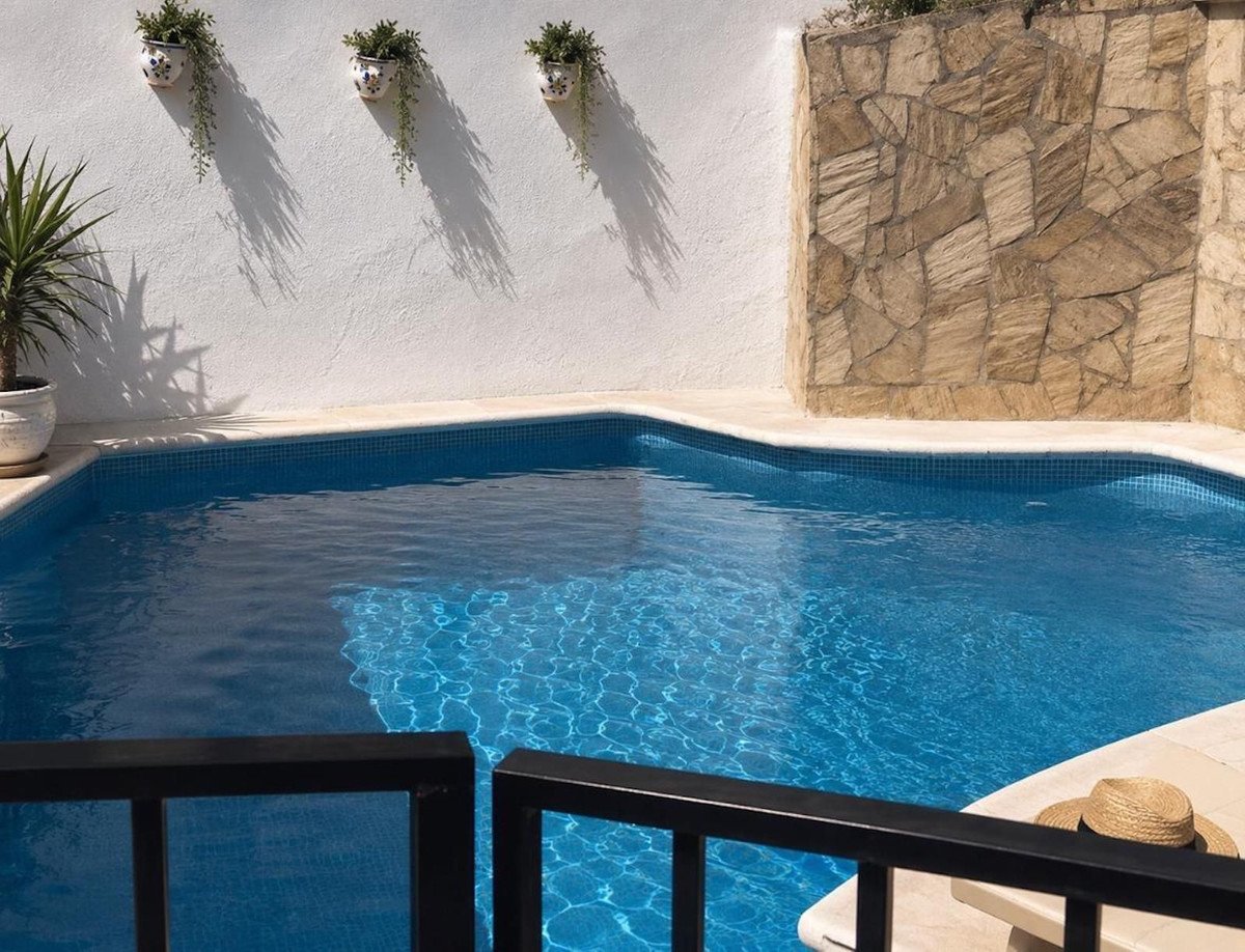 A private swimming pool with blue tiled water, surrounded by a stone wall and white wall with hanging plants.
