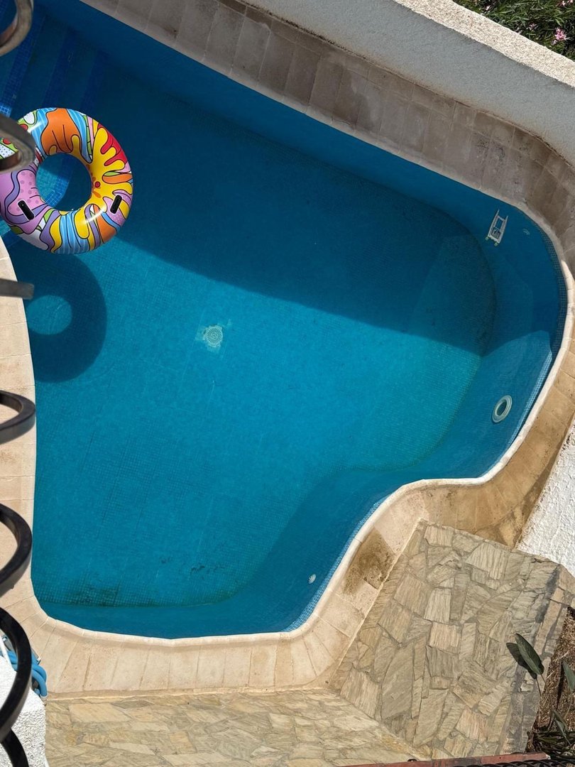 An empty swimming pool with blue water and a colorful inflatable ring floating inside. There are stone steps leading into the pool.
