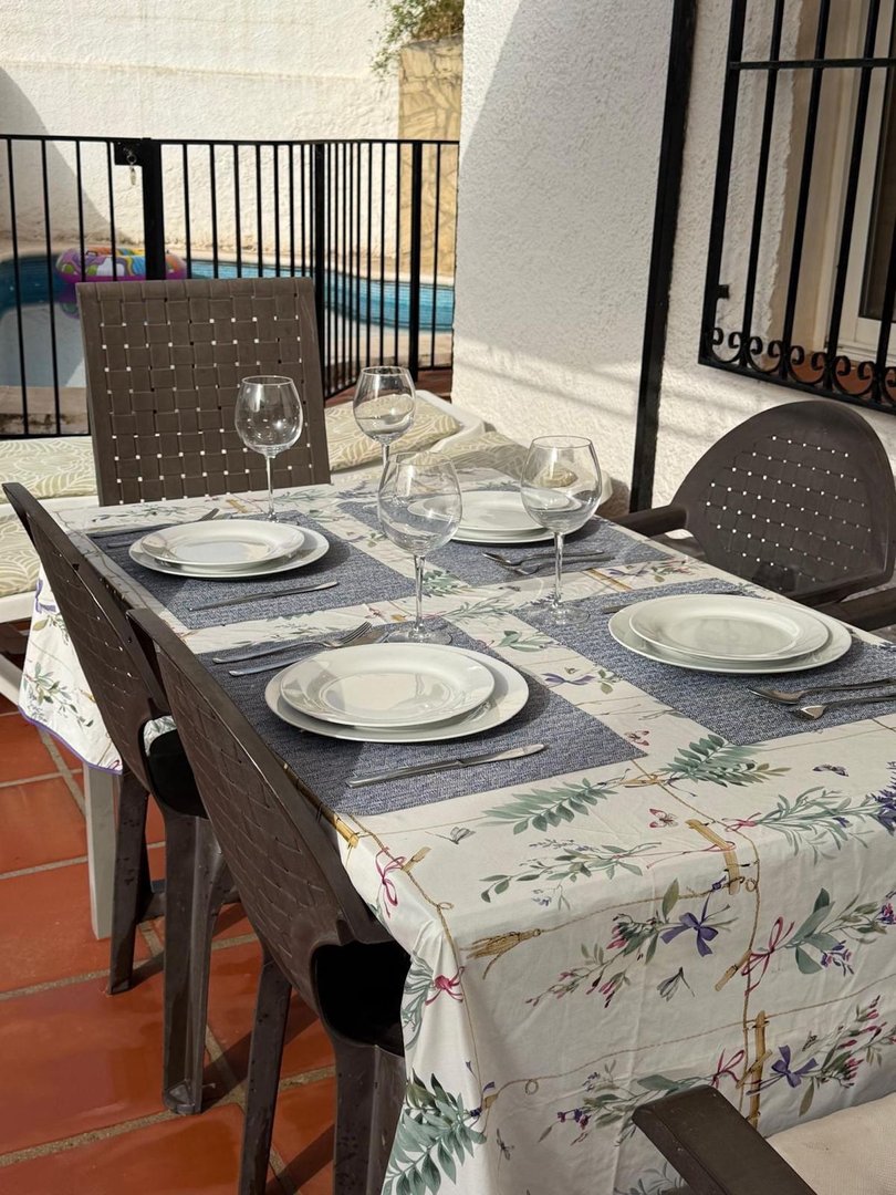 Outdoor dining table set with plates, glasses, and cutlery, overlooking a swimming pool.