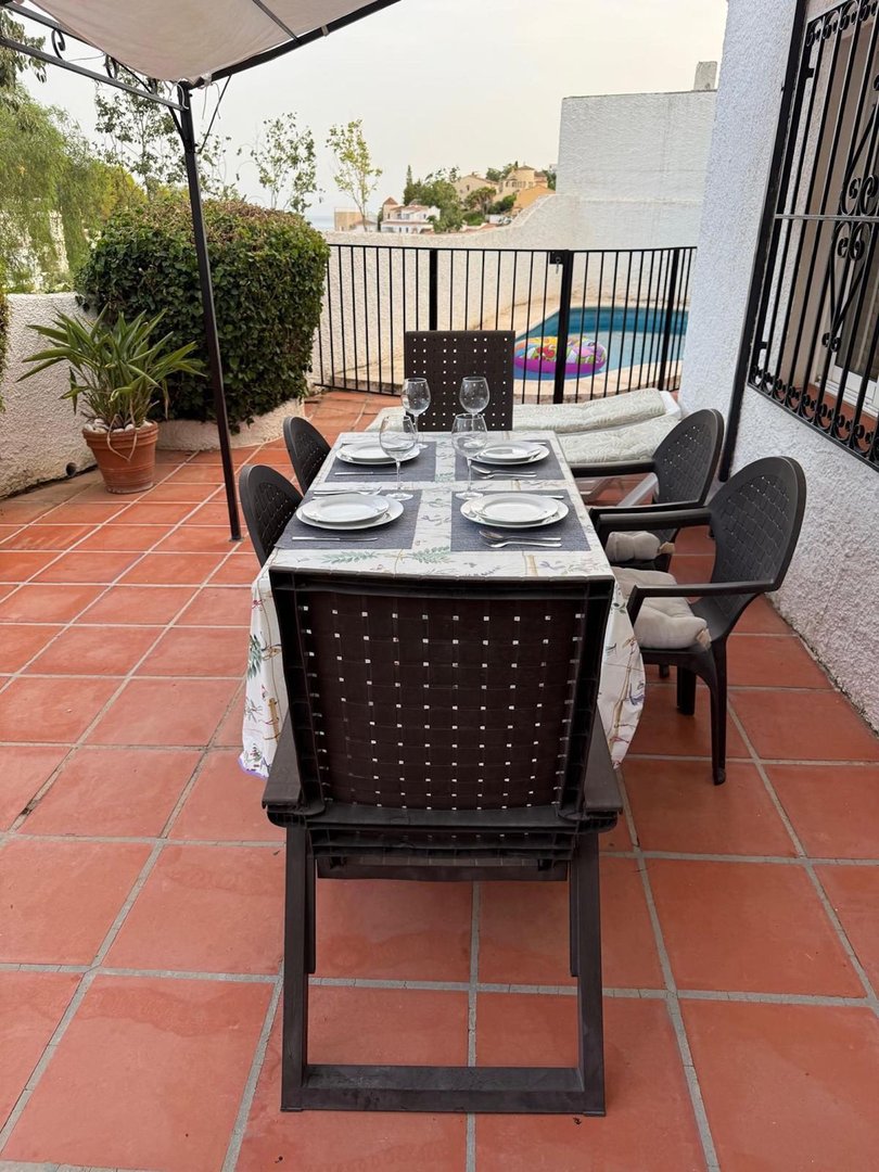 Terrace dining area with table set for four, overlooking a swimming pool and distant hillside homes.