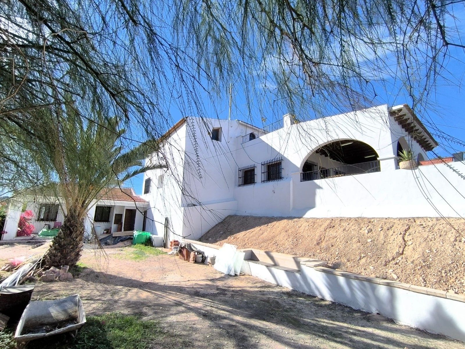 Buitenaanzicht van een wit mediterraans huis met een palmboom en blauwe lucht.