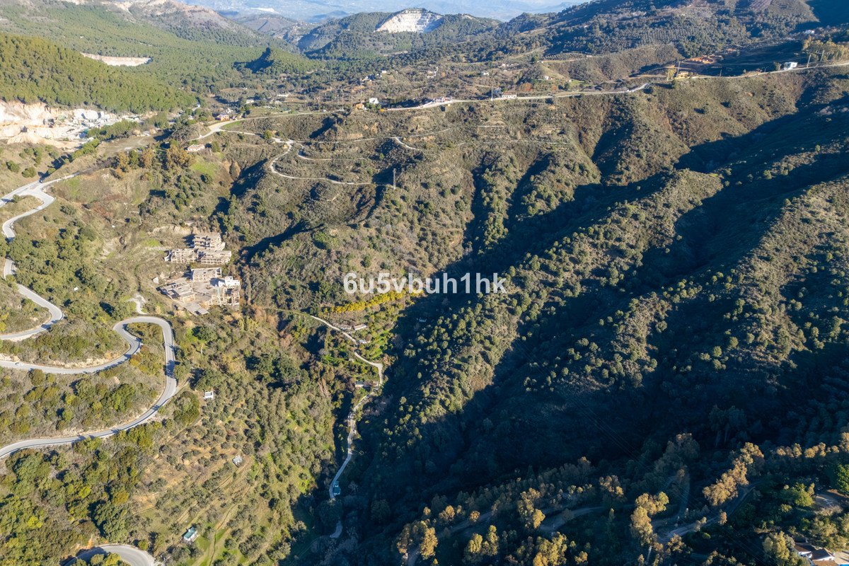 Aerial drone view of a winding road leading through a lush green mountain valley with scattered buildings.