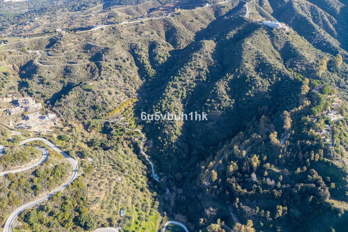 Aerial view of a sprawling estate and villas nestled on a lush, green mountainside with winding roads.