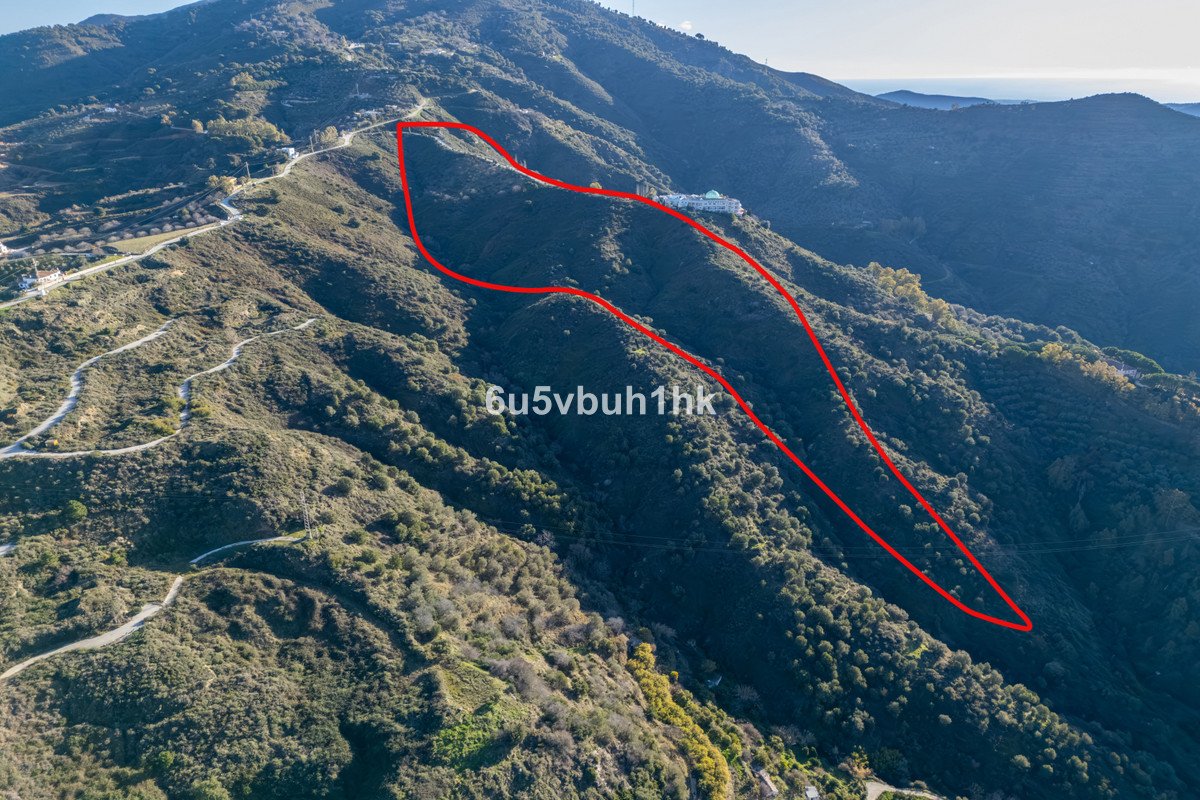 An aerial view of a white villa on a mountainside, with a red outline marking the property boundaries and a distant sea view.