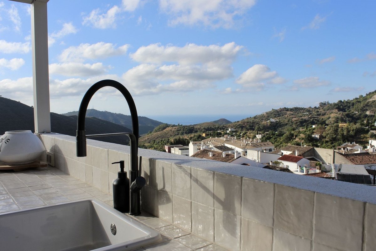 Outdoor kitchen sink with black faucet overlooking a village and the sea with mountains in the background.