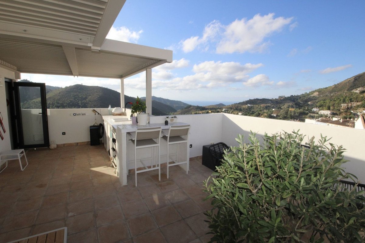 Spacious terrace with outdoor kitchen, bar stools, and a beautiful mountain view under a partly cloudy sky.