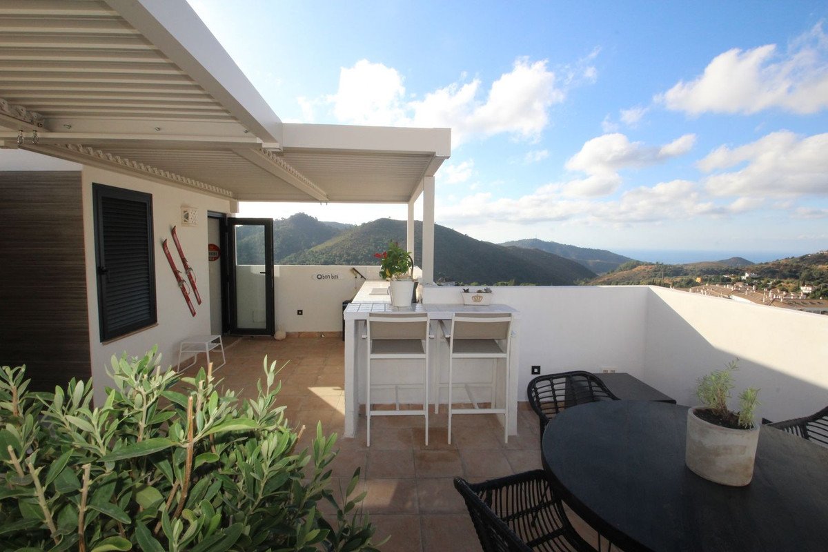 A covered terrace with seating and bar stools, offering a beautiful view of mountains and the sea.