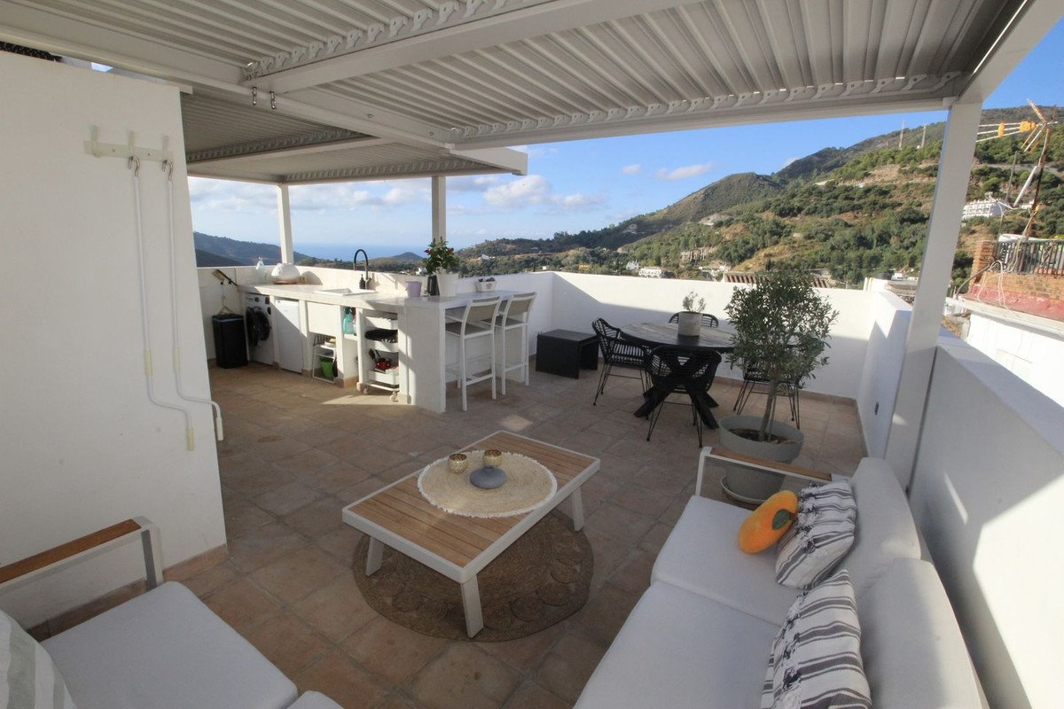 A covered terrace with an outdoor kitchen, bar, dining set, and lounge area with a view of the sea and hills.