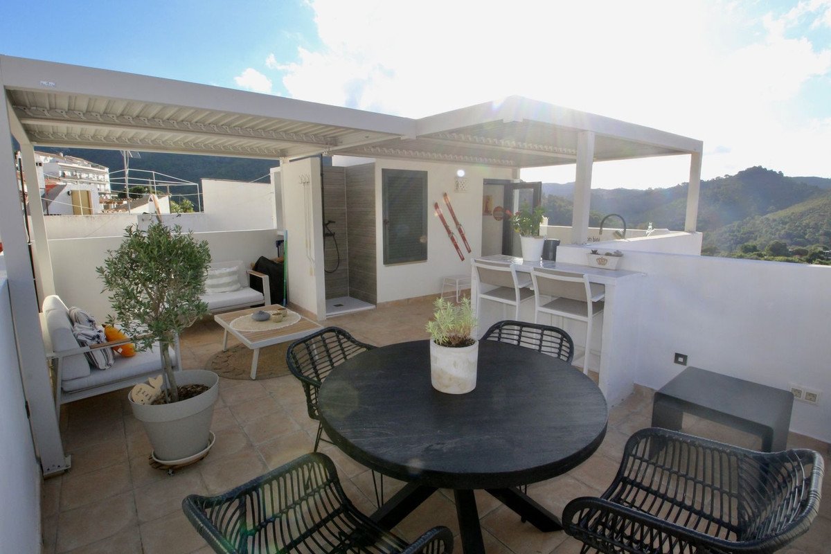 Spacious covered terrace with dining table, outdoor shower, bar area, and mountain views under a sunny sky.