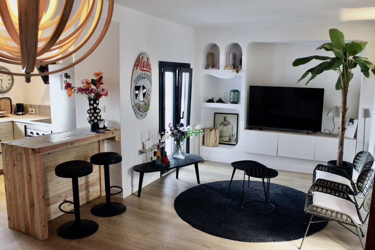 Modern living room with a wooden breakfast bar, television, and stylish seating area. Decorated with plants and art.