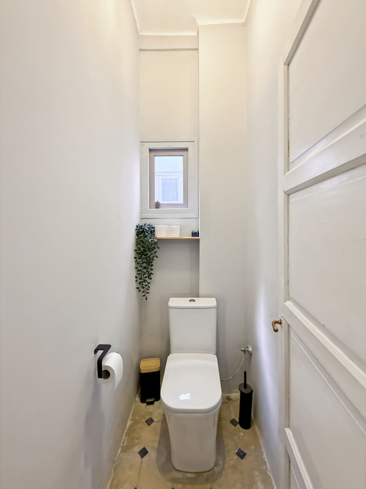 Kleine witte toiletruimte met raam en plant