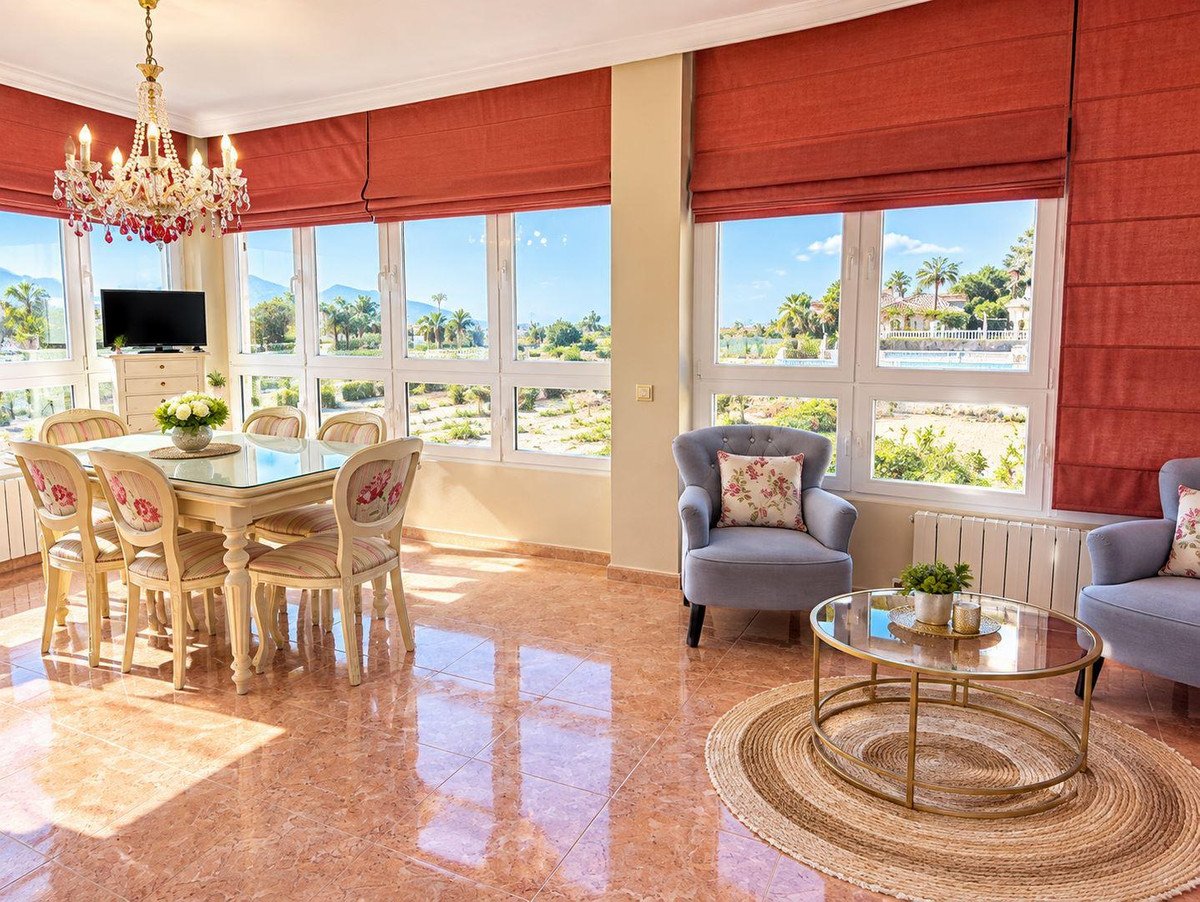 Dining area with table and chairs and a sitting area with armchairs, large windows with mountain and pool views.
