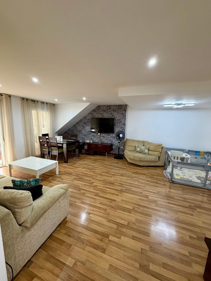 Spacious living and dining area with sofas, dining table, television, and wooden flooring.