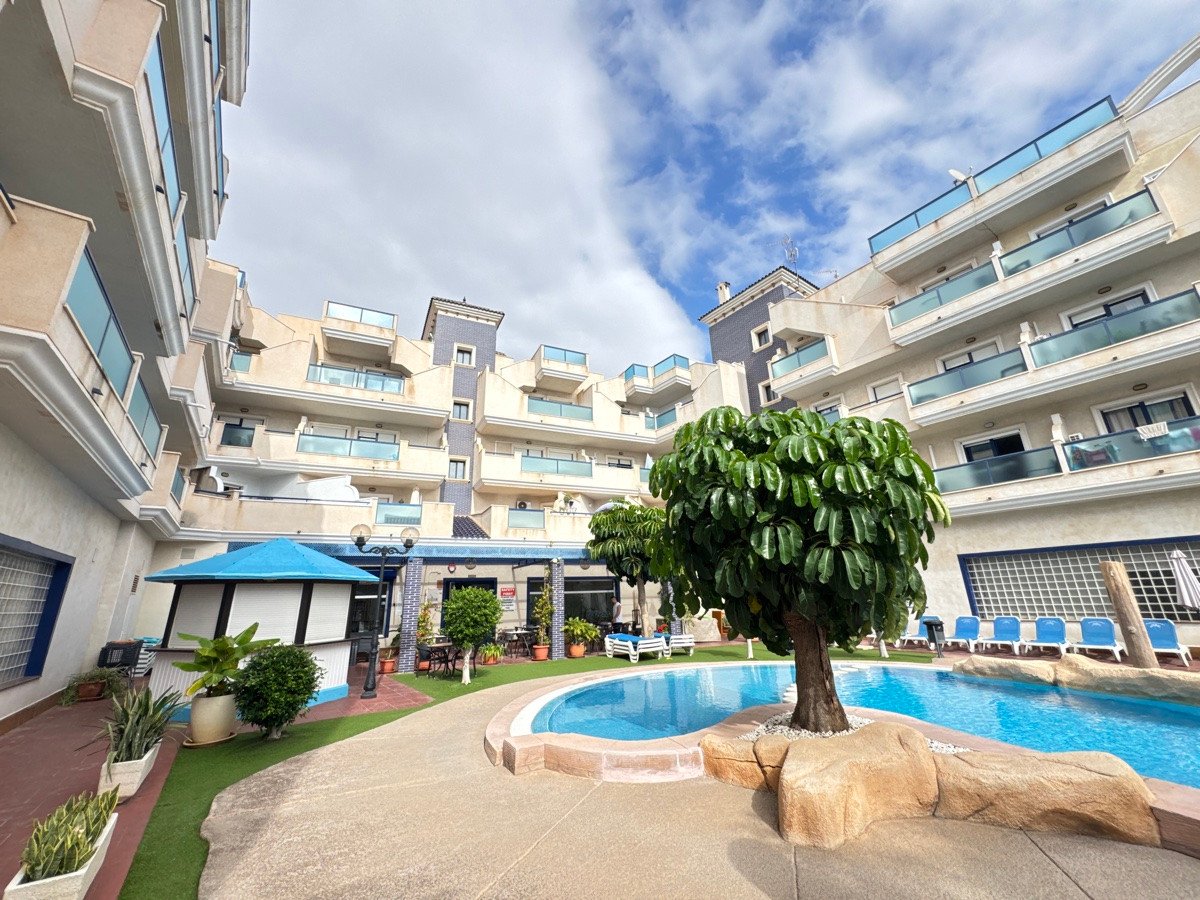 Apartment buildings surrounding a blue swimming pool with lounge chairs and a small tree in the foreground.
