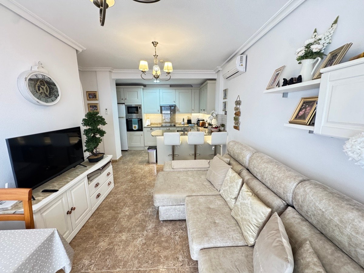 Modern open-plan living area and kitchen with comfortable sofa, TV, and breakfast bar.