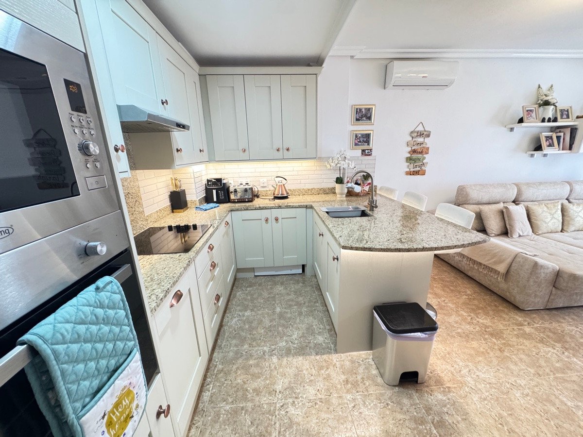 Modern U-shaped kitchen with a granite island, integrated appliances, and a spacious living area with a sectional sofa.