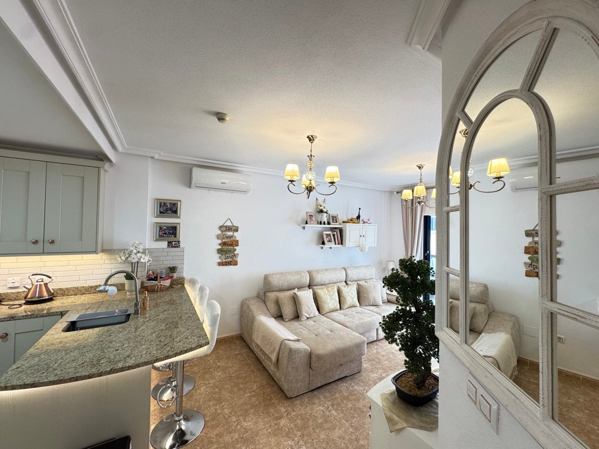 Bright and modern living area with a sectional sofa, kitchen island with bar stools, and decorative mirror.