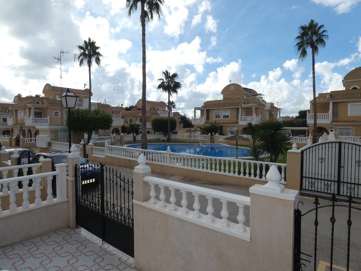 Resort apartments with a shared swimming pool and palm trees under a cloudy blue sky.