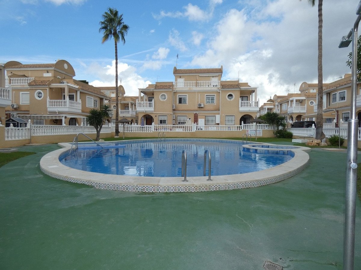A communal swimming pool with surrounding apartment buildings and palm trees on a sunny day.