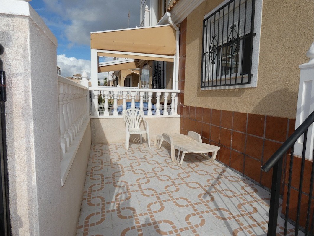 Exterior patio terrace with a white chair, sun lounger, and patterned tiles, overlooking a blue pool.