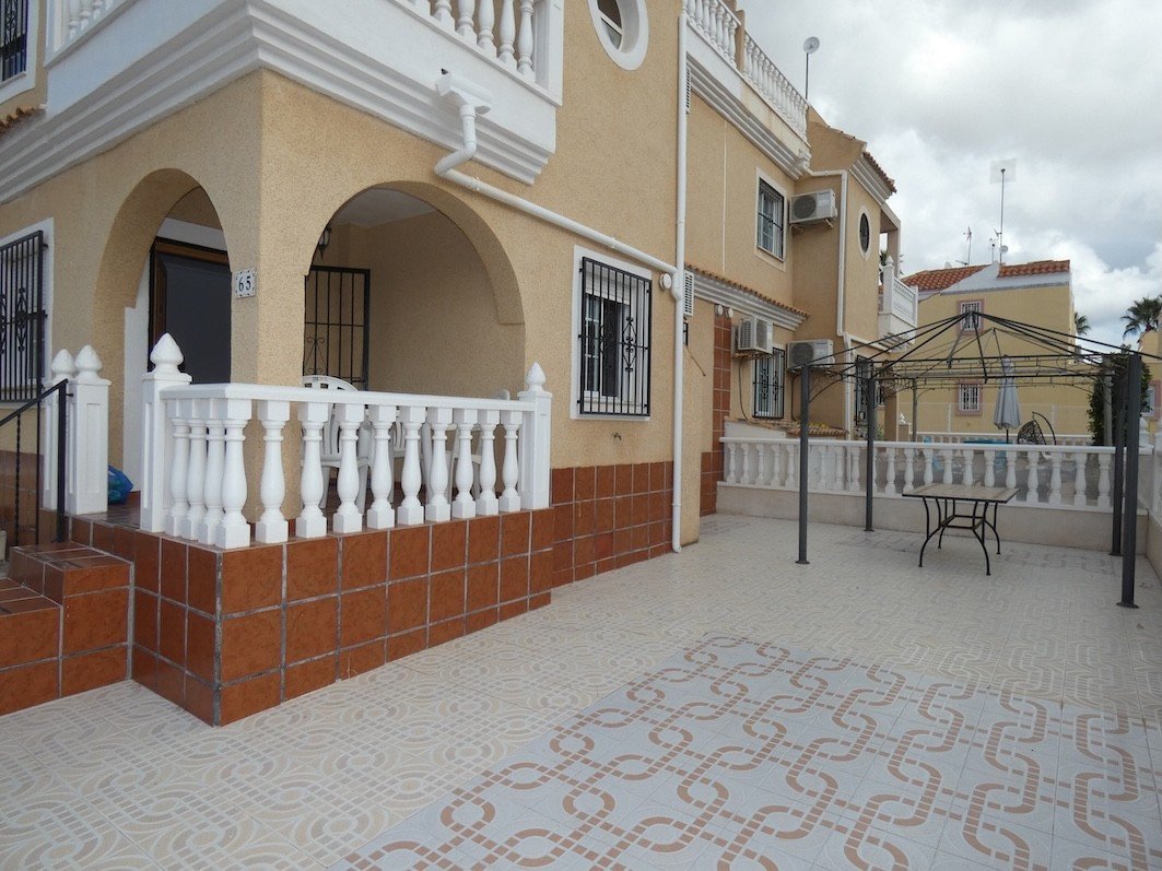 A large tiled terrace with a gazebo, table, and chairs, featuring a white balustrade and arches on the building exterior.