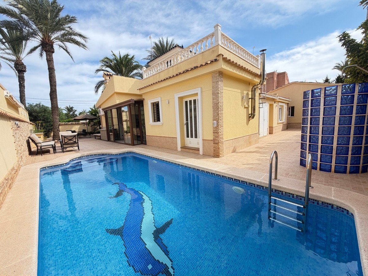 A yellow villa with a private swimming pool featuring a dolphin mosaic and a tiled patio with outdoor seating.