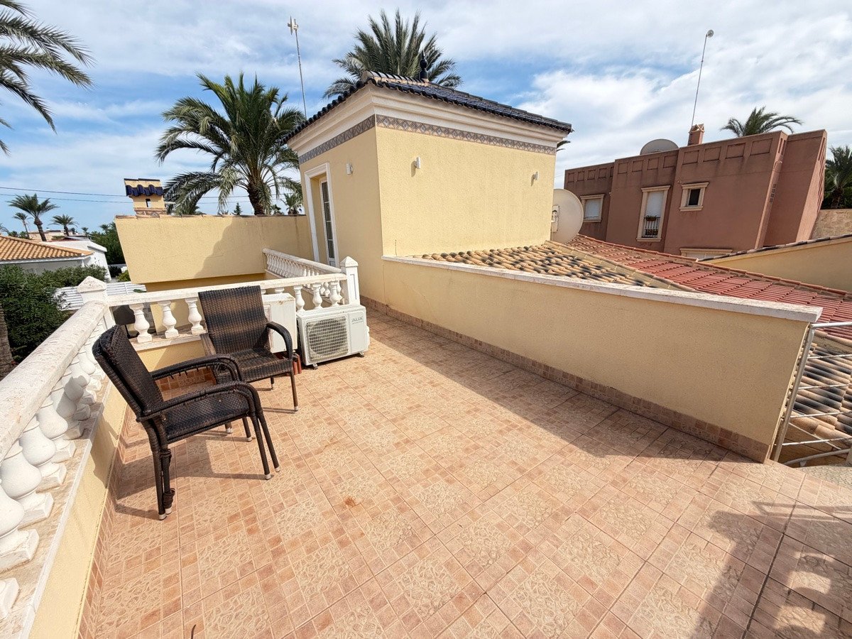 Sunny terrace with two chairs and air conditioning unit, surrounded by palm trees and overlooking rooftops.