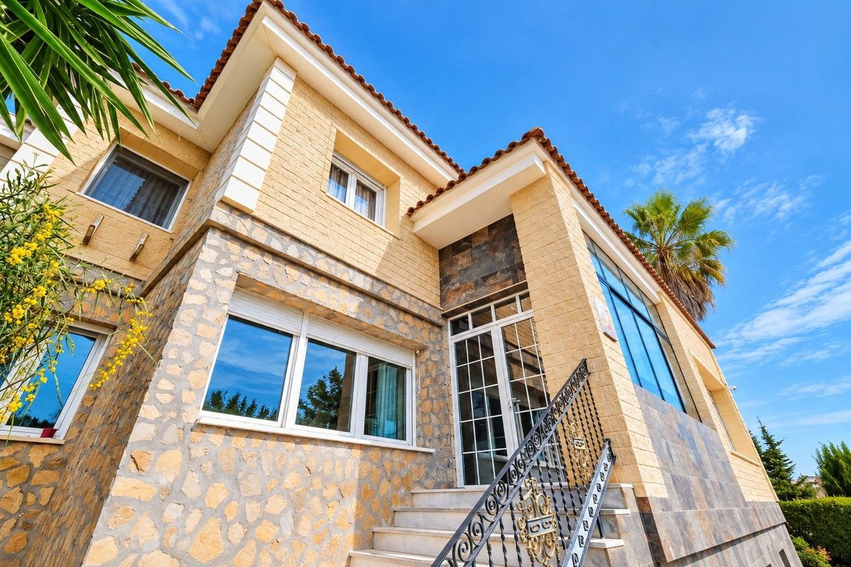 Exterior of a modern villa with light brick and stone facade, large windows, and a staircase leading to the entrance.
