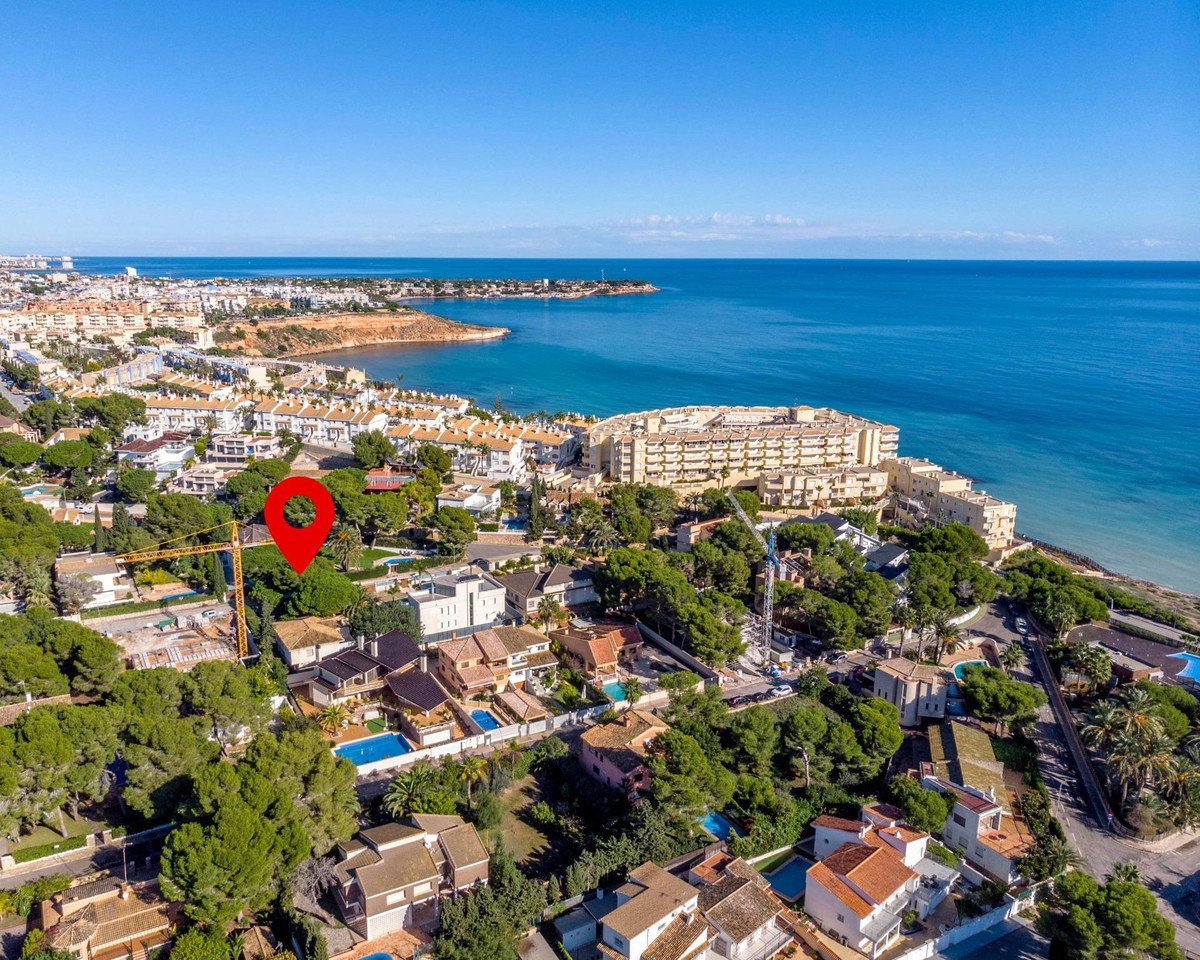 Aerial view of a coastal town with a large hotel complex and residential homes overlooking the blue sea.