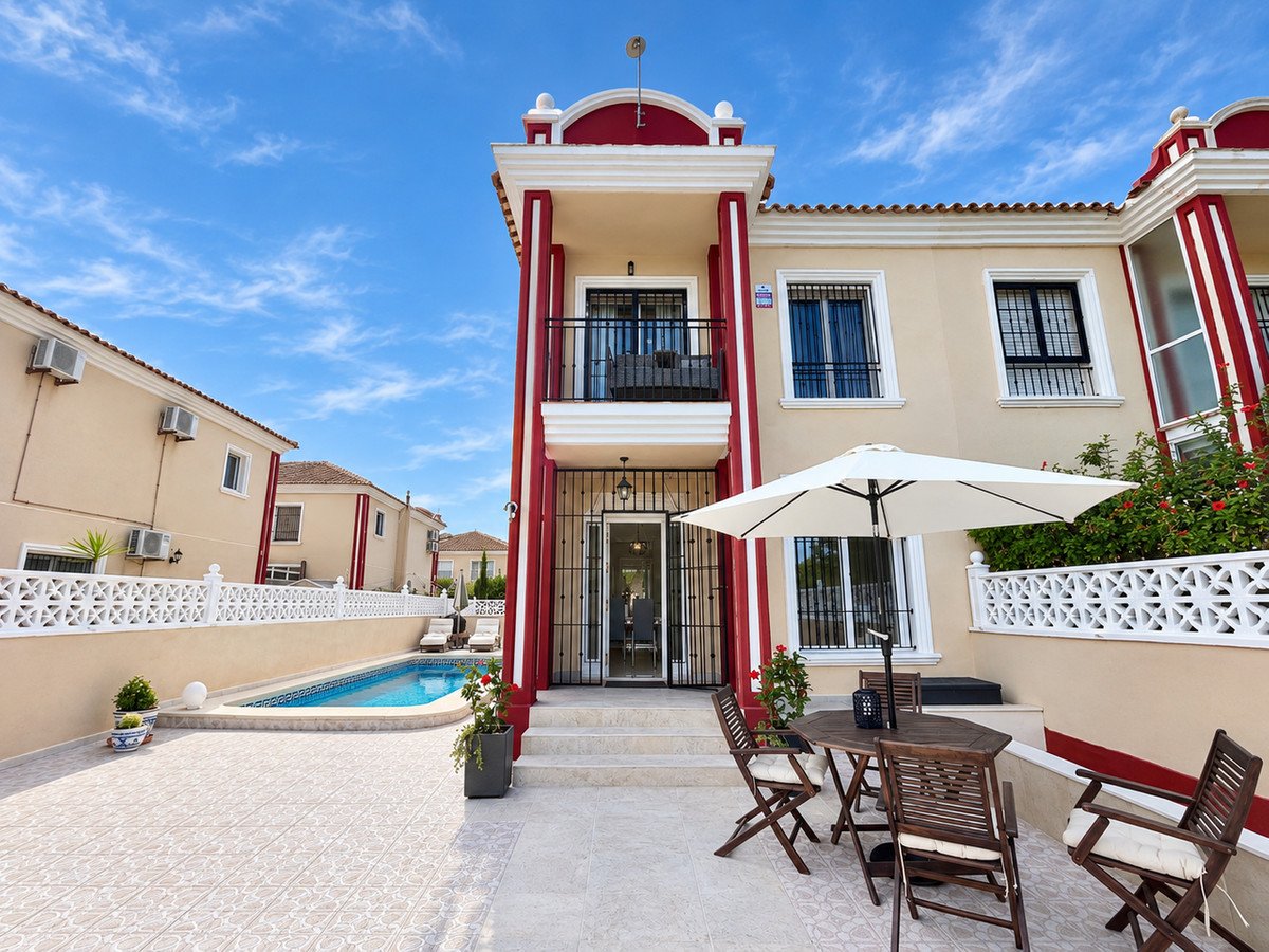 Exterior view of a villa with a private swimming pool, patio with outdoor dining furniture, and lush greenery under a blue sky.
