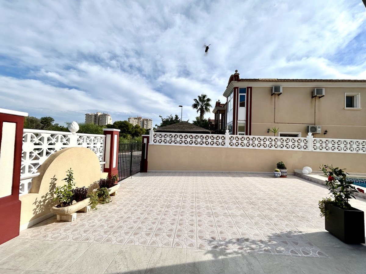 Tiled patio area with a fence, pool in the background, and a house with air conditioning units visible.