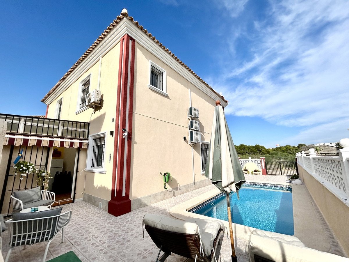 A villa with a swimming pool, outdoor seating, and a tiled patio under a blue sky.