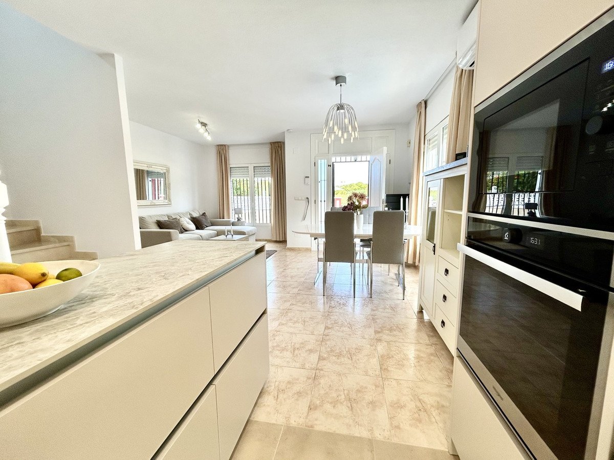 Open-plan living and dining area with modern kitchen, featuring a sofa, dining table, and large windows overlooking greenery.