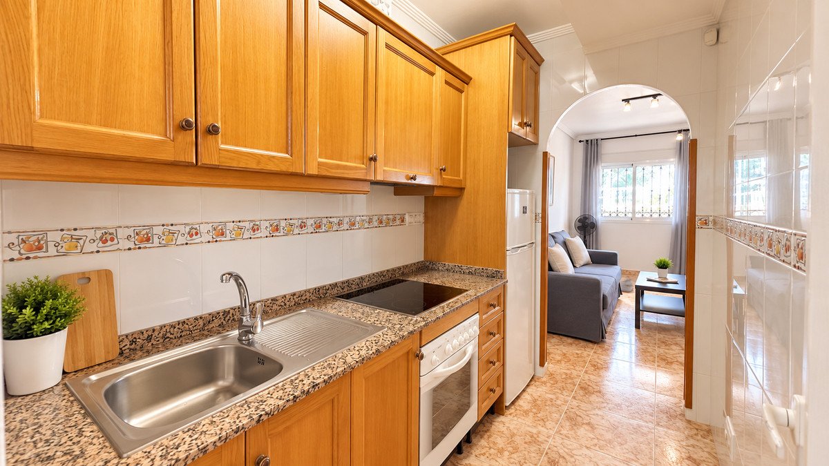 Modern kitchen with wooden cabinets and granite countertops leads to a cozy living area with a sofa and coffee table.