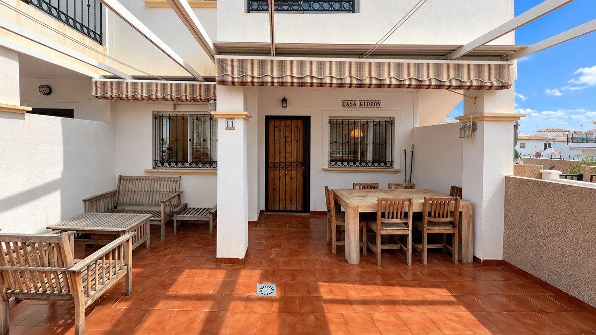 A covered terrace with outdoor dining set and lounge seating, featuring awnings and views of rooftops.