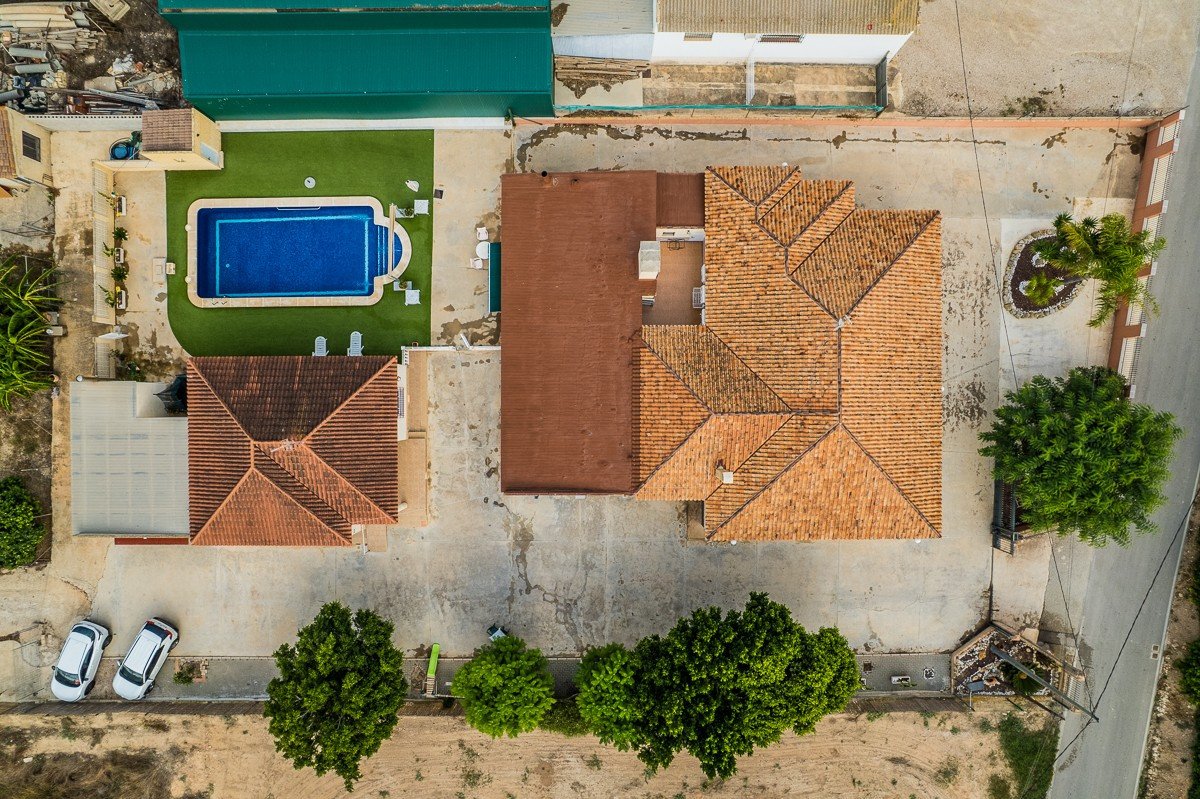 Aerial view of a house with a swimming pool, surrounded by trees, and two cars parked outside.