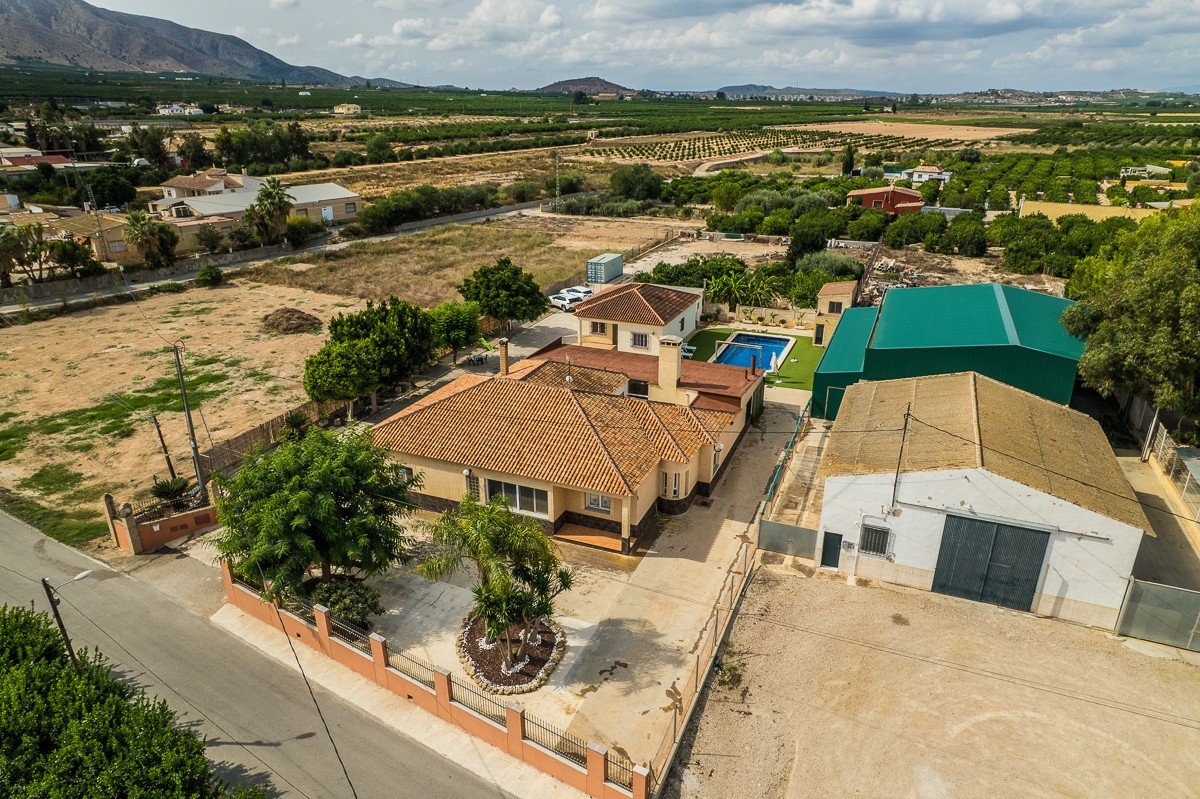 Aerial view of a house with a swimming pool and surrounding fields, offering a rural landscape view.