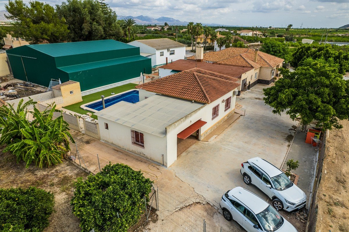 Aerial view of a villa with a blue swimming pool, artificial turf, and two cars parked in the driveway.