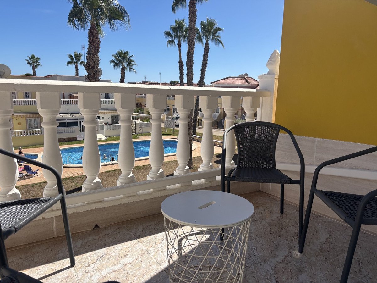 Balcony with seating overlooking a swimming pool with palm trees and clear blue sky.