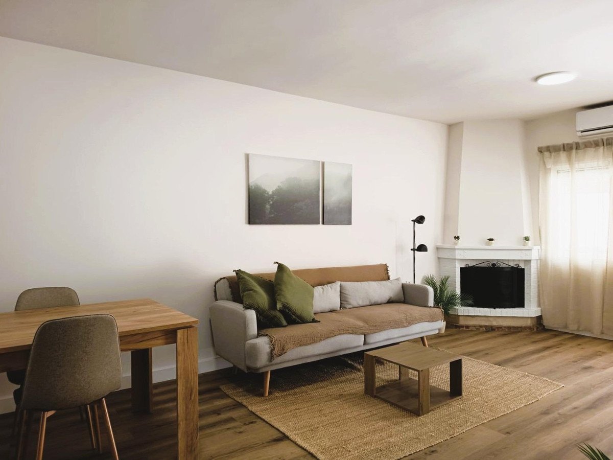 A modern living room features a sofa, coffee table, fireplace, dining table, and artwork on the wall.