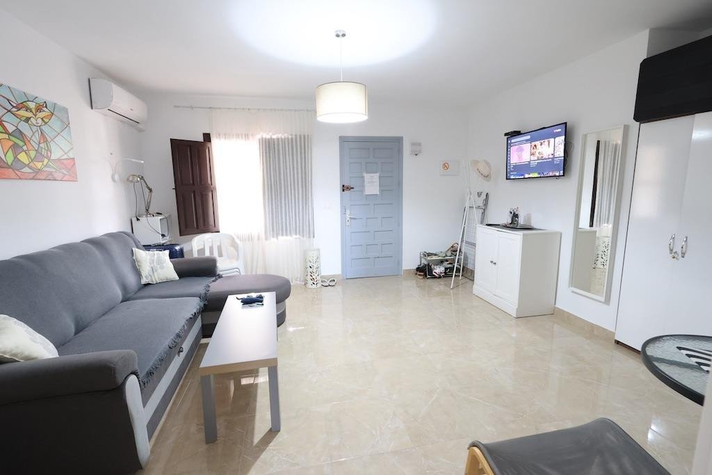 Spacious living room with a large grey sofa, coffee table, television, and a door leading outside.