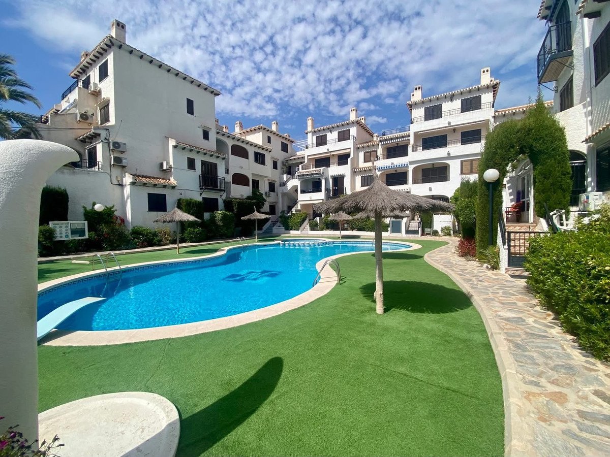 A swimming pool with artificial grass and surrounding apartment buildings on a sunny day.
