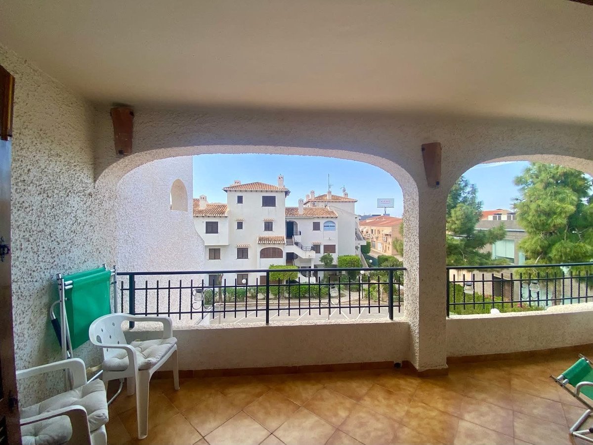 Terrace with chairs and view of apartment buildings and trees under a clear blue sky.