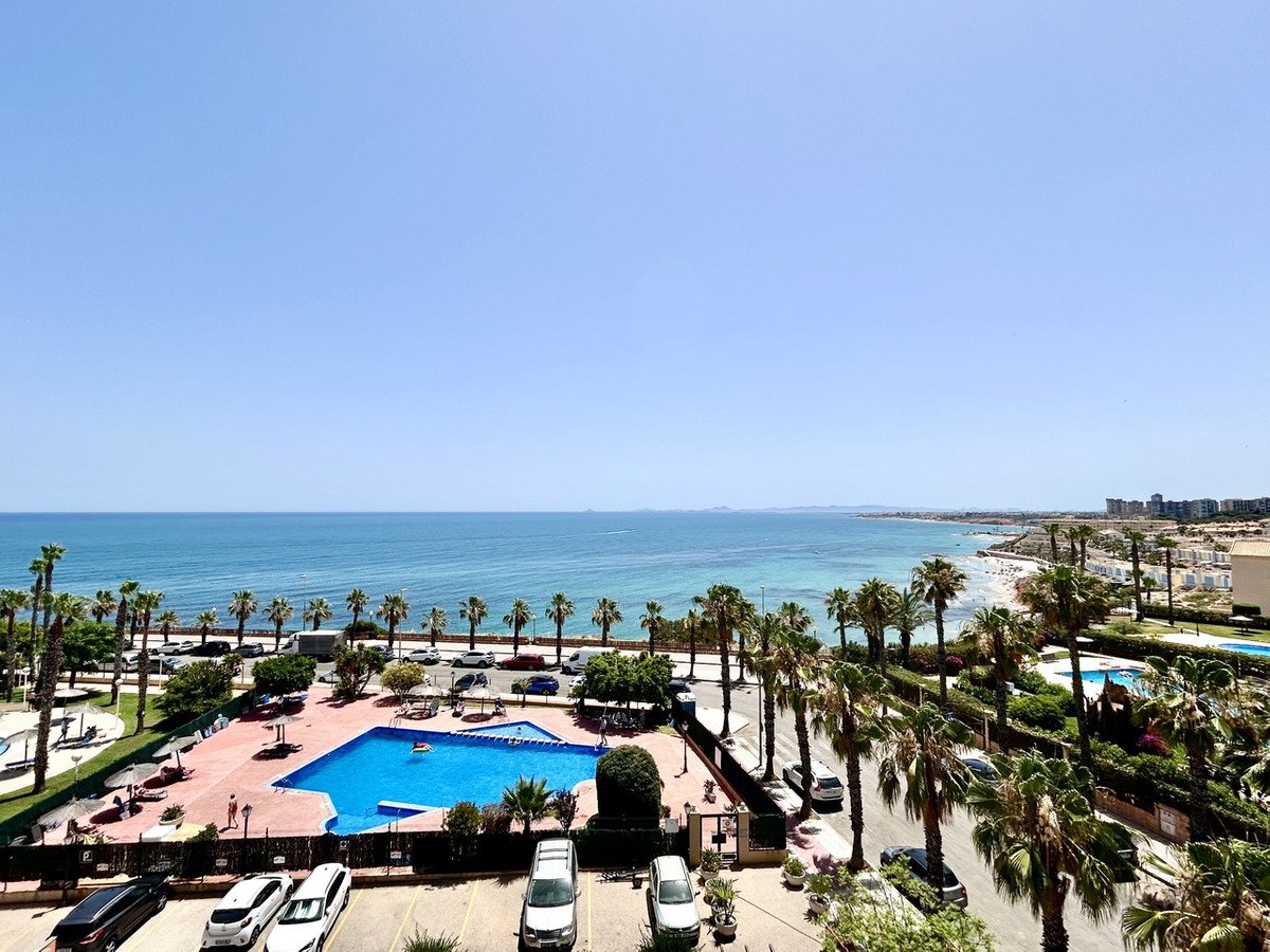 Balcony view of the sea with palm trees, a swimming pool, and beach area.